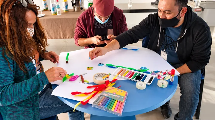 Participantes crean dibujos y composiciones de colores alrededor de una mesa