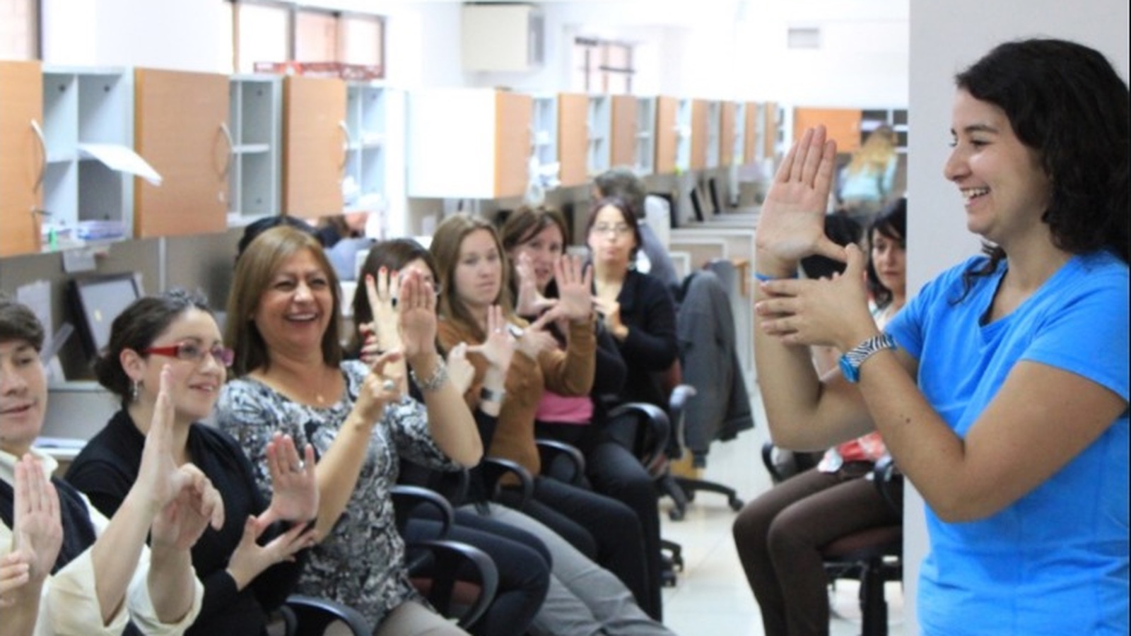 Facilitadora guía una actividad de movimiento a personas sentadas en una oficina